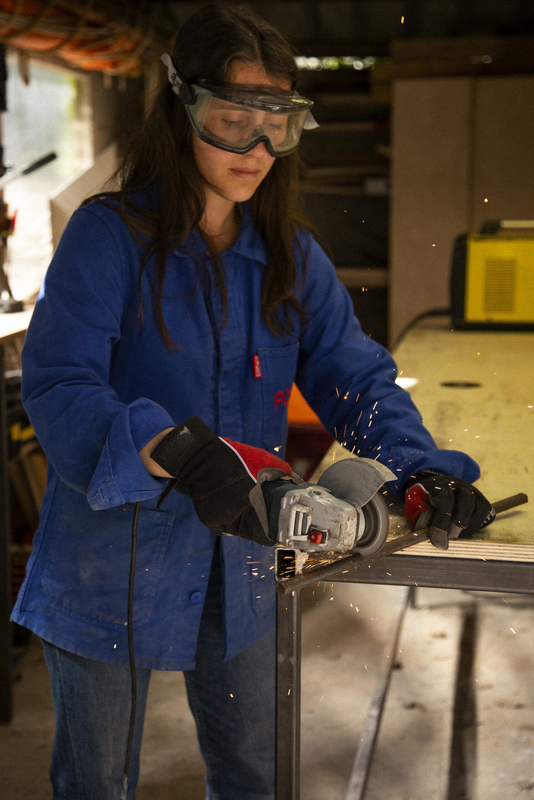 Photo d'une artisane meulant une pièce de métal dans son atelier.
